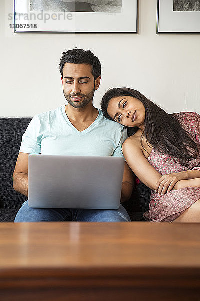 Paar benutzt Laptop-Computer  während es zu Hause auf dem Sofa sitzt