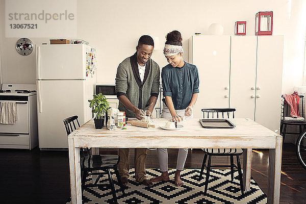 Lächelndes Paar knetet Teig bei Tisch in der Küche