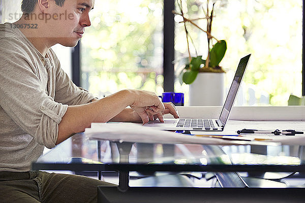 Seitenansicht eines ernsthaften Mannes  der einen Laptop am Tisch im Büro benutzt
