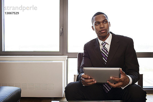 Mann mit Tablet-Computer schaut weg  während er im Büro sitzt