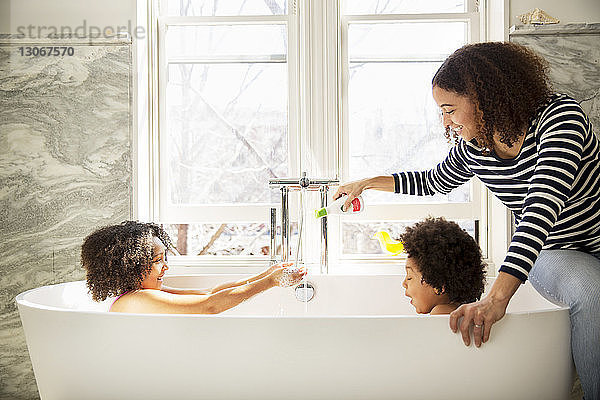 Frau gießt Seife ein  während Kinder in der Badewanne spielen
