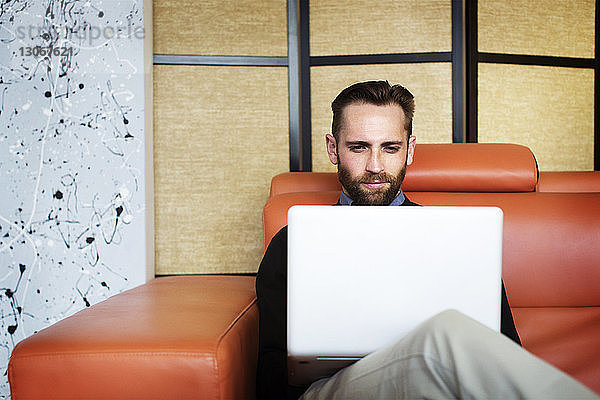 Mann benutzt Laptop-Computer  während er im Büro auf dem Sofa sitzt