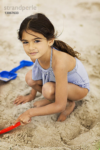 Porträt eines lächelnden Mädchens beim Spielen mit Sand am Strand