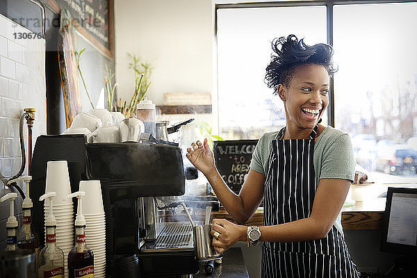 Glückliche Frau schaut beim Kaffeekochen im Café weg