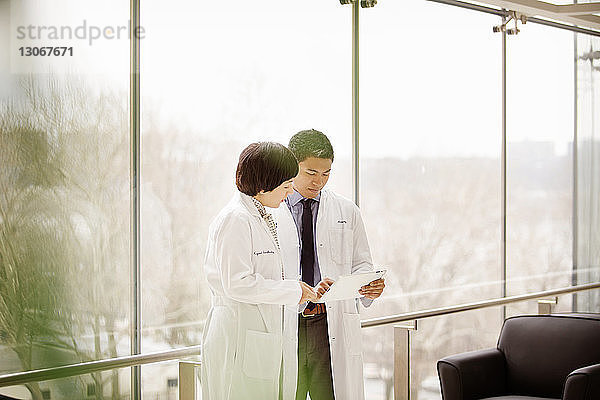 Ärzte schauen in Tablet-Computer  während sie im Krankenhaus am Fenster stehen