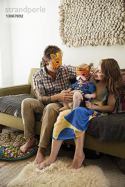 Glückliche Familie mit Maske zu Hause auf dem Sofa sitzend
