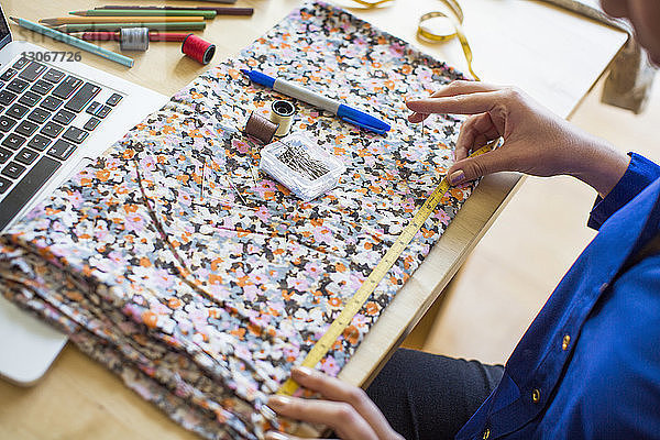 Beschnittenes Bild eines Modedesigners  der am Schreibtisch Stoff misst