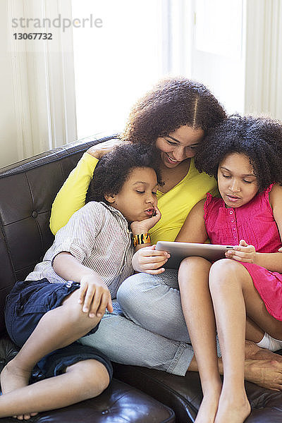 Hochwinkelansicht einer Familie  die einen Tablet-Computer benutzt  während sie zu Hause auf dem Sofa sitzt