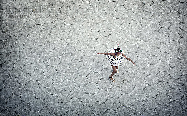 Draufsicht auf ein tanzendes Mädchen auf einer Pflasterstraße in der Stadt