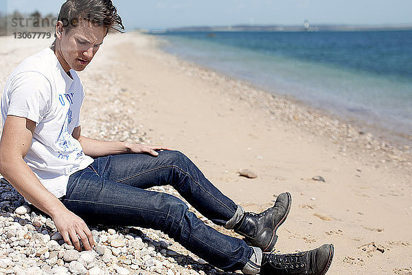 Mann schaut nach unten  während er am Strand am Ufer sitzt