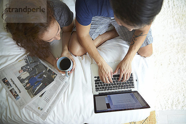 Frau trinkt Kaffee im Liegen  während ein Mann einen Laptop im Bett benutzt