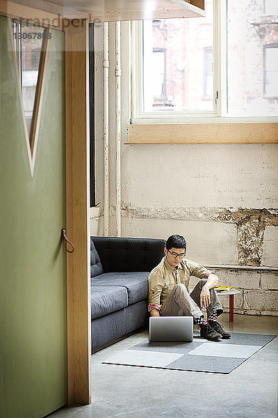 Geschäftsmann benutzt Laptop-Computer  während er im Büro auf dem Boden sitzt