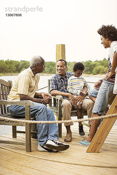 Mehrgenerationen-Familie unterhält sich beim Entspannen am Pier vor klarem Himmel