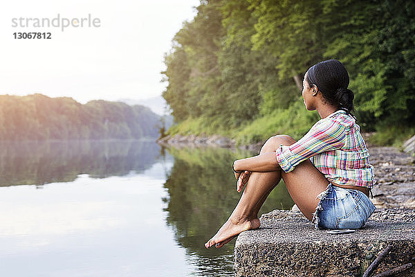 Seitenansicht einer Frau  die auf einem Felsen gegen einen See im Wald sitzt