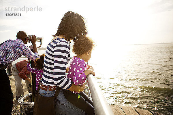 Familie schaut auf den Fluss  während sie bei Sonnenschein am Geländer der Promenade steht