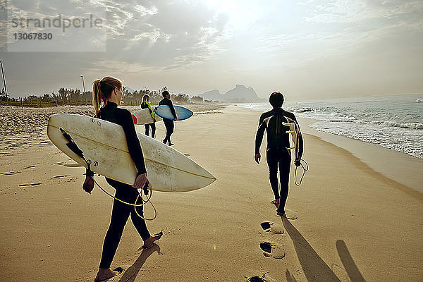 Freunde tragen Surfbretter  wenn sie am Strand auf Sand laufen