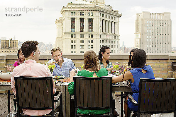 Freunde unterhalten sich beim Essen am Tisch auf der Gebäudeterrasse in der Stadt