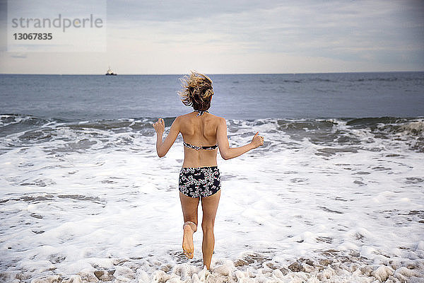 Rückansicht einer Frau  die am Strand an der Küste läuft
