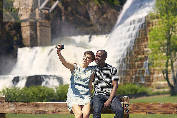 Paar  das sich beim Sitzen auf dem Geländer gegen den Wasserfall selbstständig macht