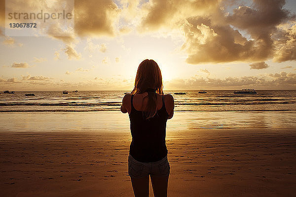 Rückansicht einer Frau  die bei Sonnenuntergang am Strand steht