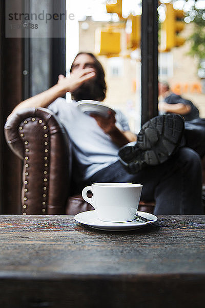 Kaffeetasse auf Tisch mit im Hintergrund sitzendem Mann