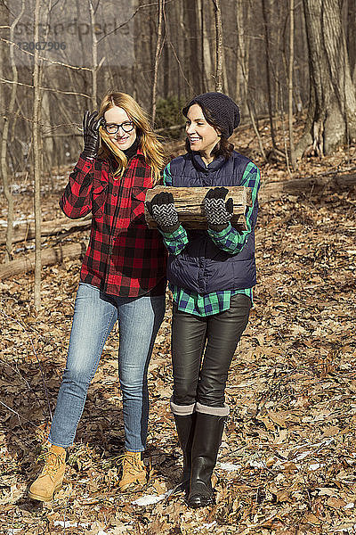 Frau trägt Brennholz  während sie mit einem Freund im Wald spazieren geht