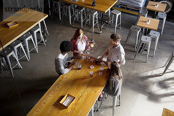 Draufsicht auf Freunde beim Kartenspielen bei einem Bier am Tisch in einer Brauerei
