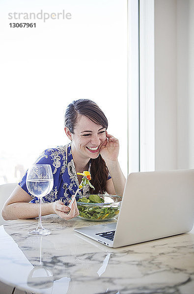 Lächelnde Frau schaut beim Frühstück auf Laptop-Computer