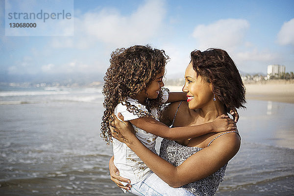 Mutter trägt Tochter  während sie am Strand am Ufer steht