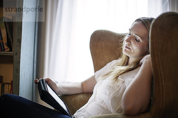 Frau schaut auf Tablet-Computer  während sie auf einem Sessel sitzt