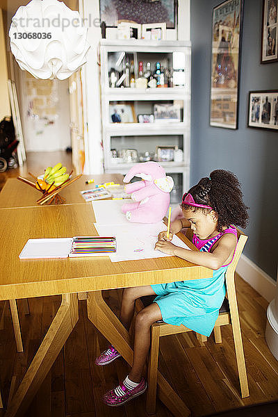Hochwinkelansicht eines Mädchens  das zu Hause am Tisch sitzt und auf Papier zeichnet