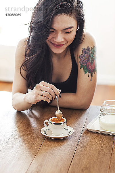 Frau rührt Kaffee mit einem Löffel um  während sie zu Hause am Tisch sitzt