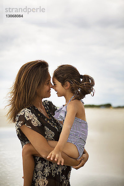 Mutter und Tochter reiben sich die Nasen  während sie am Strand stehen