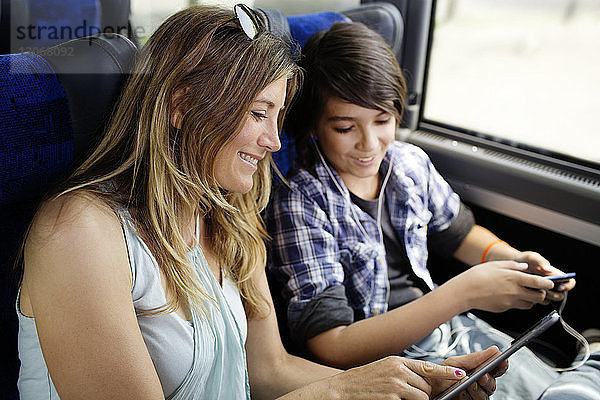 Mutter und Sohn schauen auf Tablet-Computer  während sie im Bus sitzen