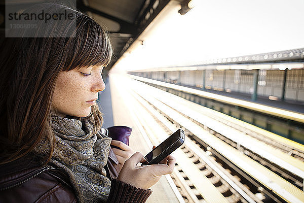 Frau benutzt Smartphone am Bahnhof