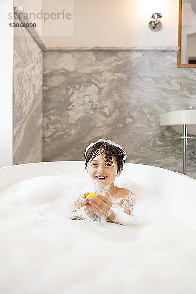 Porträt eines Jungen  der beim Baden in der Badewanne eine Gummiente hält