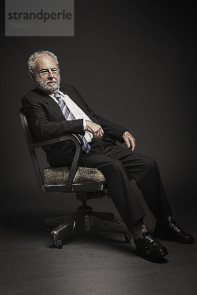 Porträt eines hochrangigen Geschäftsmannes  der auf einem Bürostuhl sitzt  vor schwarzem Hintergrund