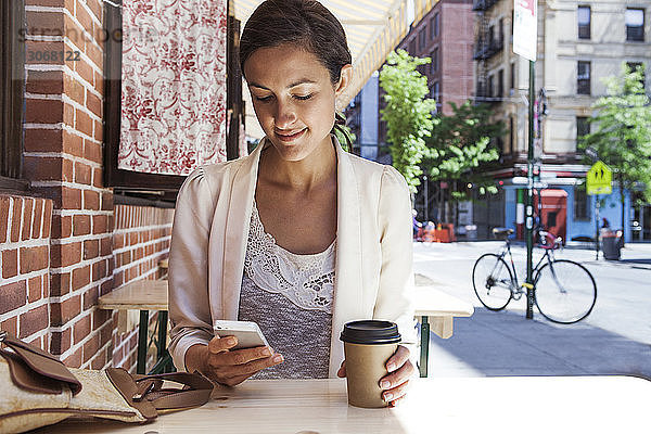 Frau benutzt Smartphone  während sie im Straßencafé sitzt