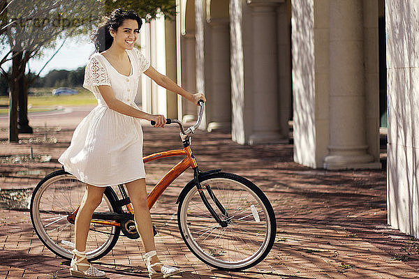 Glückliche Teenagerin geht an einem sonnigen Tag mit dem Fahrrad