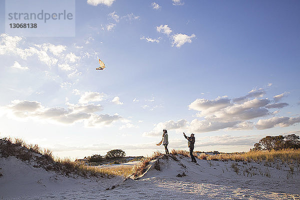 Mann mit Freundin lässt Drachen steigen  während er auf Sanddünen steht