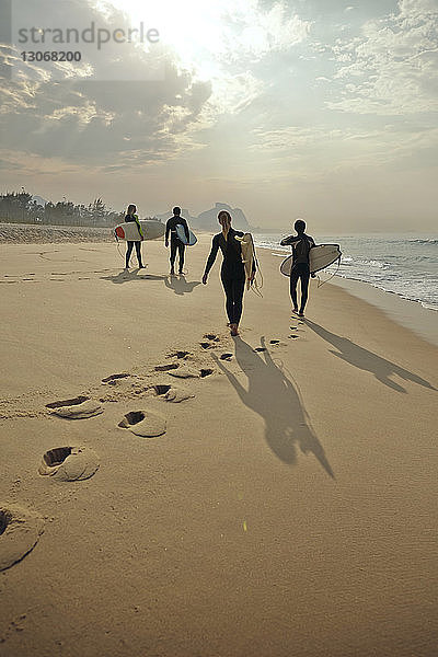 Rückansicht von Freunden  die Surfbretter tragen  während sie am Strand auf Sand laufen