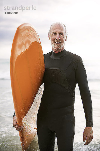 Porträt eines älteren Mannes mit Surfbrett im Meer stehend