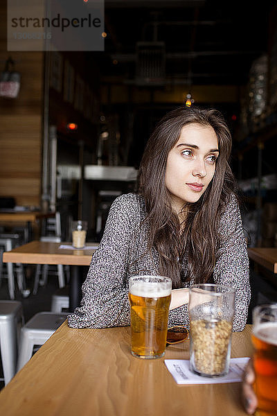 Nachdenkliche Frau trinkt Bier  während sie in einer Brauerei am Tisch sitzt