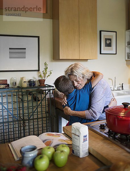 Glückliche Frau umarmt Enkel  während sie zu Hause in der Küche steht