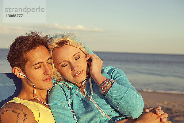 Paar entspannt sich beim Musikhören mit Kopfhörer am Strand