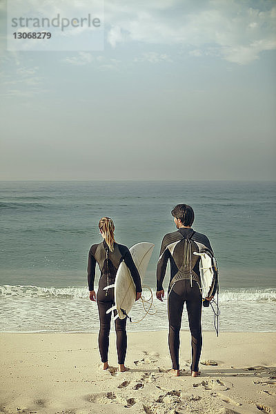 Rückansicht eines Paares  das Surfbretter trägt  während es am Ufer steht