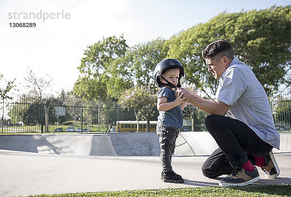 Seitenansicht des Vaters  der dem Sohn beim Helmtragen im Skateboard-Park hilft