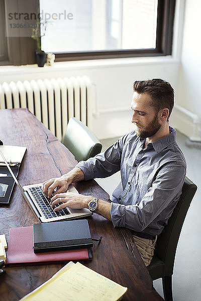 Hochwinkelansicht eines Geschäftsmannes mit Laptop-Computer  während er im Büro sitzt