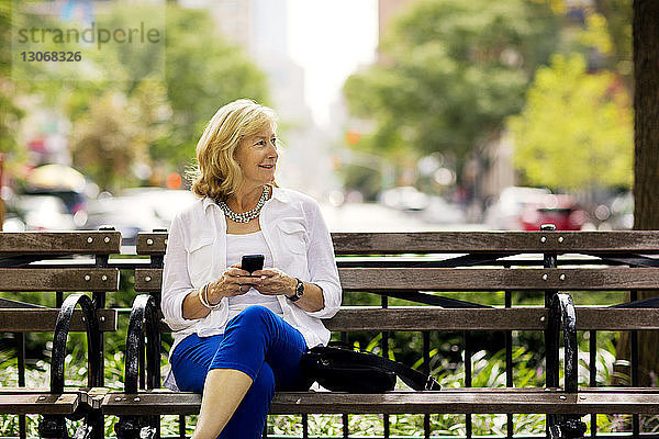 Frau schaut weg  während sie in der Stadt ein Mobiltelefon benutzt