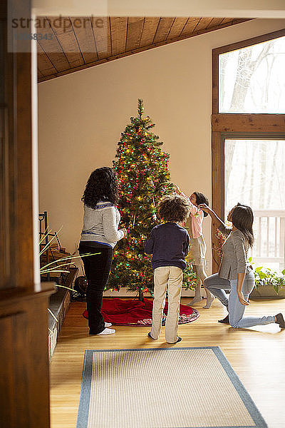 Familie schmückt zu Hause den Weihnachtsbaum am Fenster